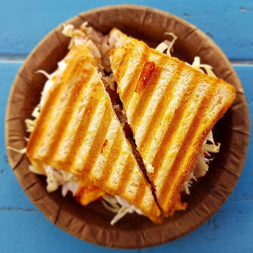 Grilled sandwich halves with shredded filling in a brown paper bowl on a blue table.
